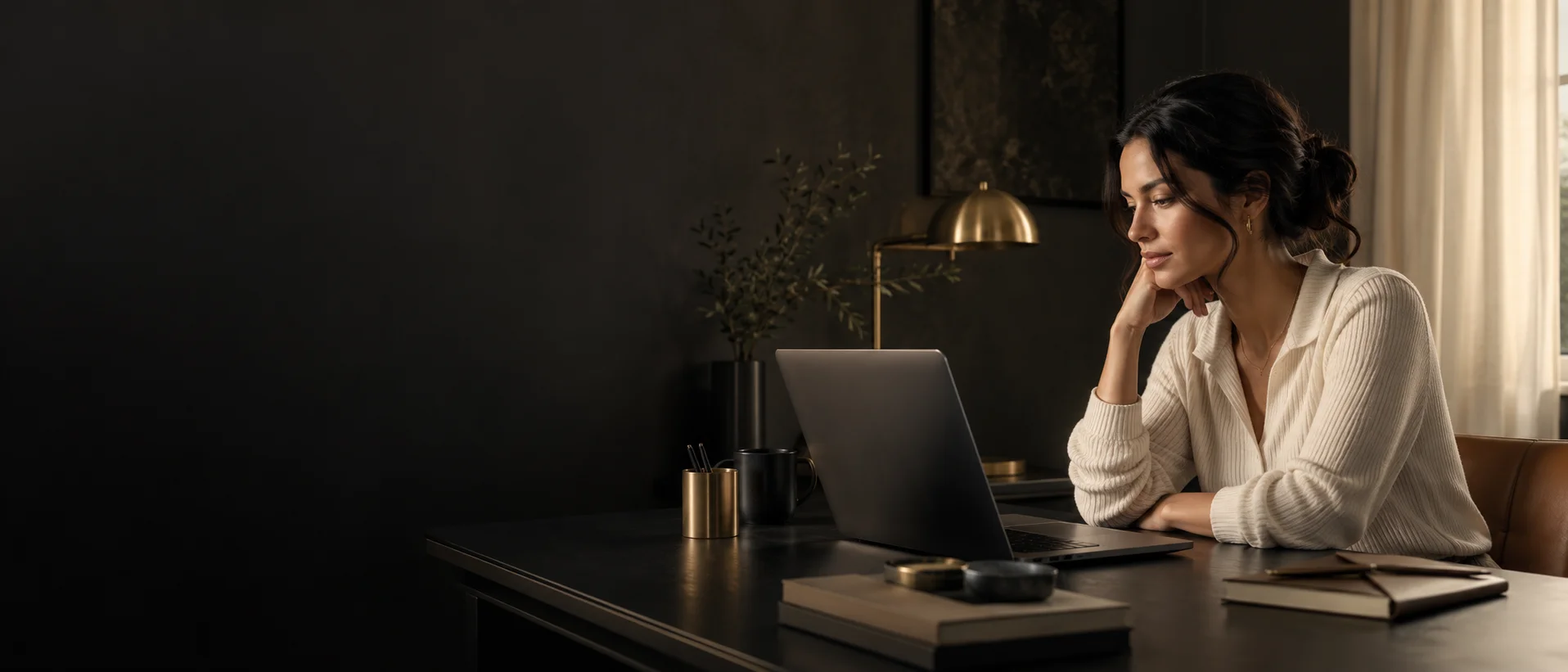 Woman working at a laptop in a dark, warmly lit home workspace